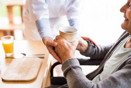 Eine Pflegekraft reicht einem alten Menschen am Tisch einen Trinkbecher