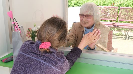 In der Klön-Bude sitzen eine ältere und eine jüngere Frau. Sie reden miteinander und legen ihre Hände aneinander.
