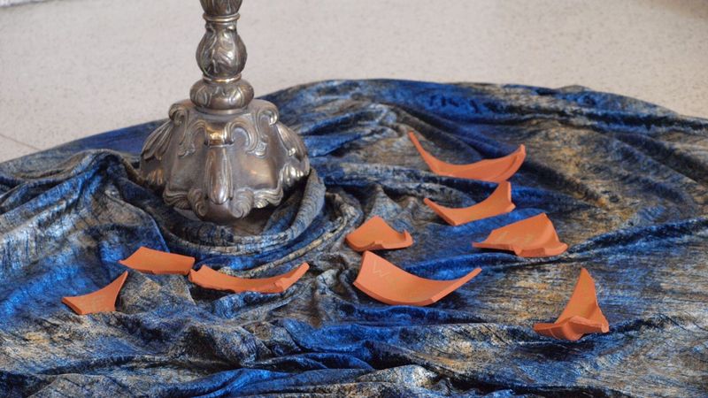ZUm Gedenken an Verstorbene: Tonscherben auf einem blaugrauen Samttuch am Fuß eines Kerzenständers