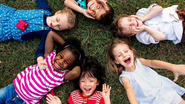 Sechs Kinder liegen sternförmig auf dem Rasen.
