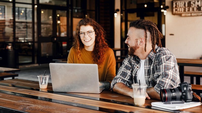 Eine junge Frau und ein junger Mann sitzen zusammen am Tisch und arbeiten an einem Laptop.