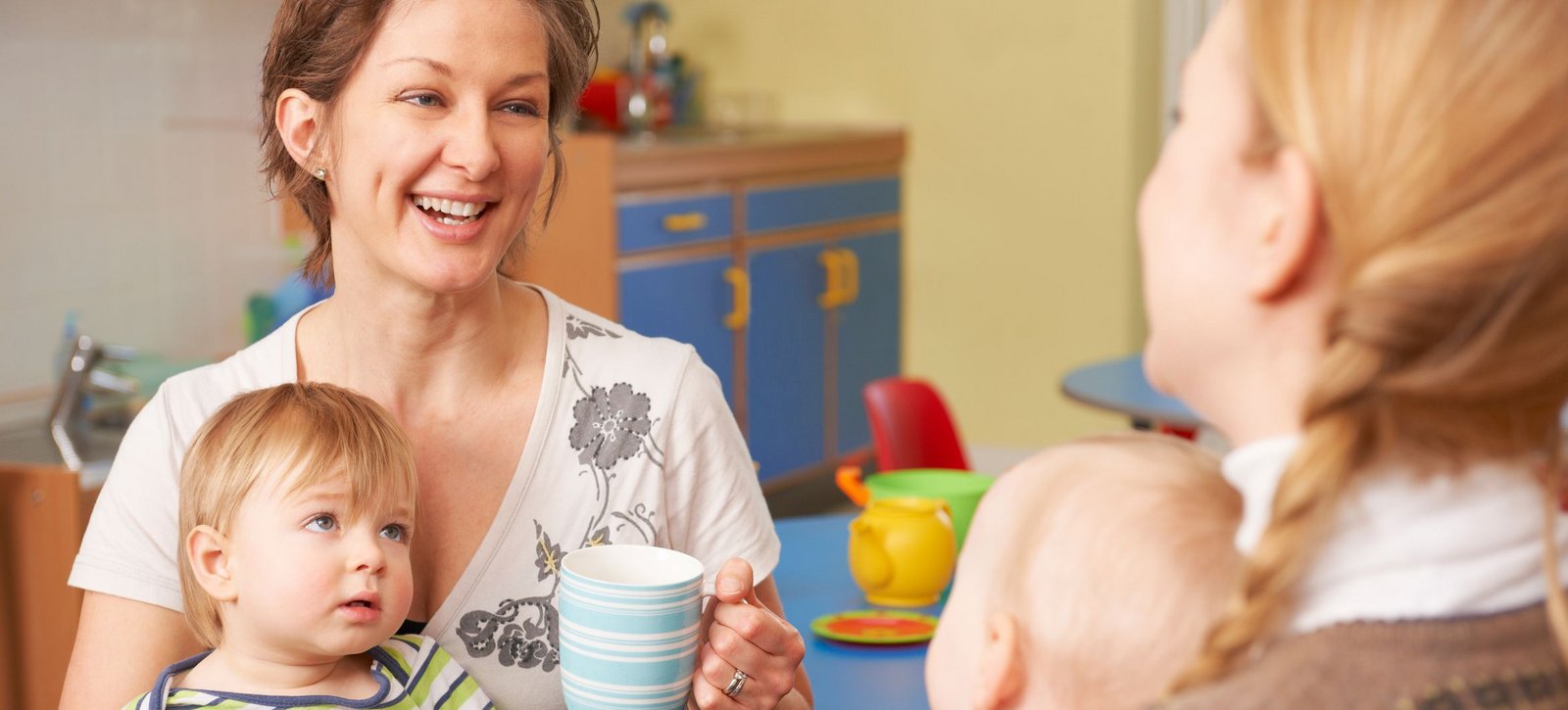 Zwei junge Mütter mit ihren Babys auf dem Schoß unterhalten sich