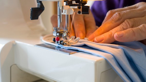 Eine Person näht mit einer Nähmaschine.
