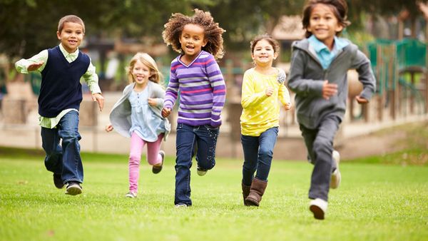 Fünf Kinder laufen über grünen Rasen.
