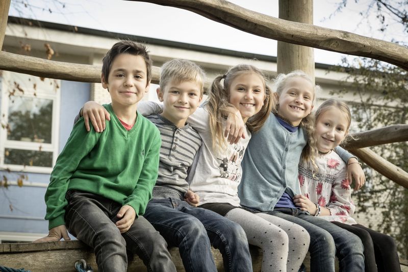 Fünf Grundschulkinder sitzen nebeneinander auf einer Mauer.