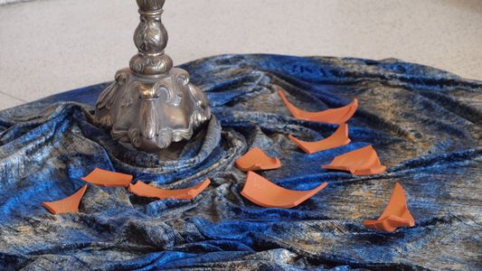 ZUm Gedenken an Verstorbene: Tonscherben auf einem blaugrauen Samttuch am Fuß eines Kerzenständers