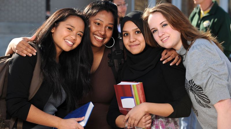 Vier junge Studentinnen umarmen sich und blicken in die Kamera.