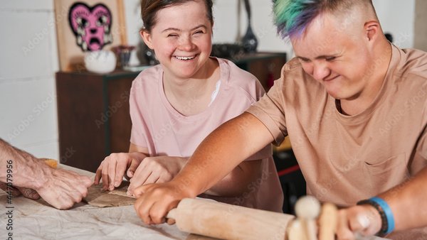 Zwei fröhliche junge Menschen mit Down-Syndrom beim gemeinsamen Töpfern und Modellieren mit Ton.