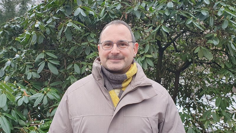 Björn Kotte steht vor einem gründen Strauch und lächelt.