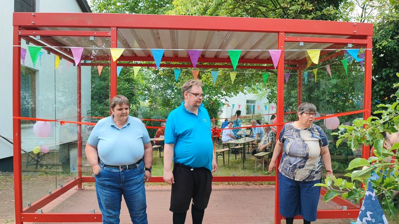 Drei Menschen steht vor dem neuen Wartehäuschen.