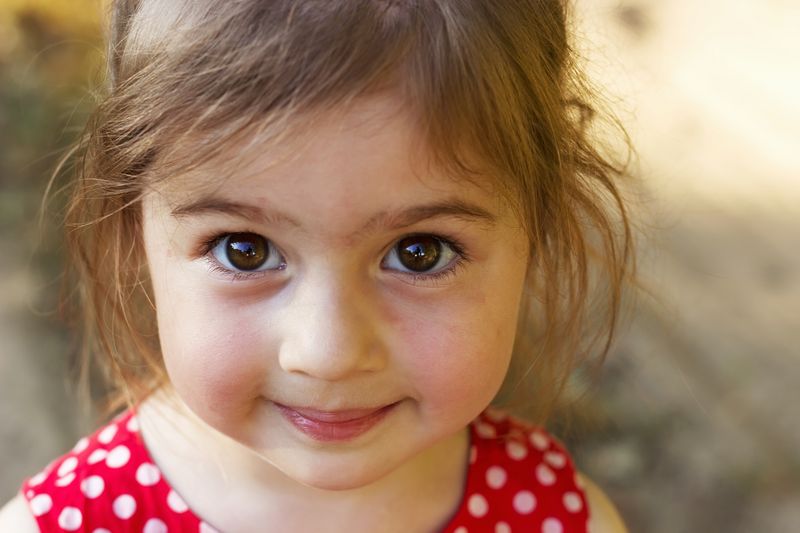 Kleines Kindergartenmädchen mit großen braunen Augen guckt.