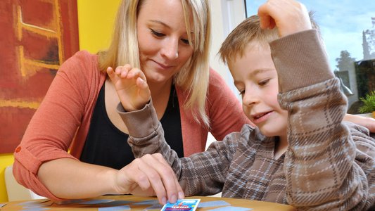 Eine junge Frau und ein Junge sitzen am Tisch und spielen Memory