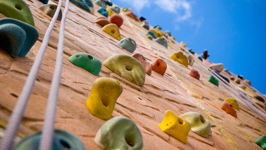 Blick von unten an einer Kletterwand entlang, darüber blauer Himmel