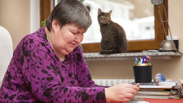 Frau mit Behinderung sitzt am Tisch und spielt Karten. Eine Katze sitzt auf der Fensterbank.