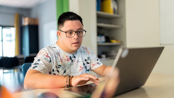 Junger Mann mit Down-Syndrom vorm Rechner