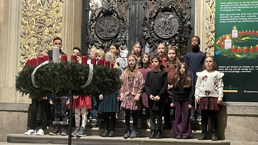 Eine Gruppe Kinder singt vor dem großen Adventskranz im Rathaus.