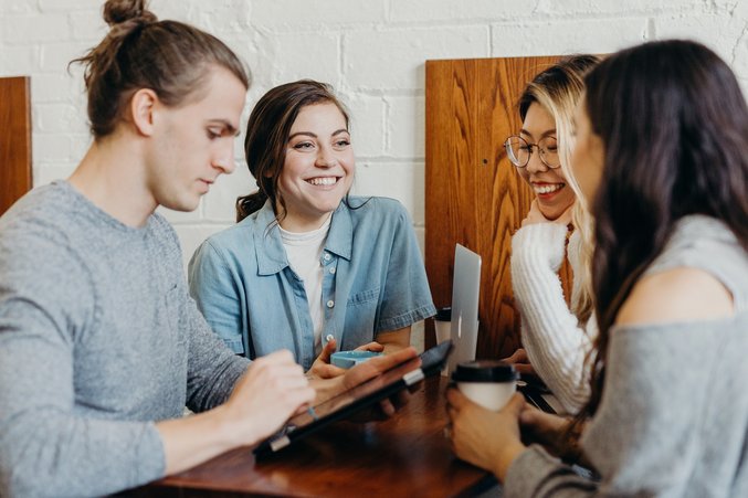 Drei Studentinnen und ein Student sitzen im Café und reden miteinander.