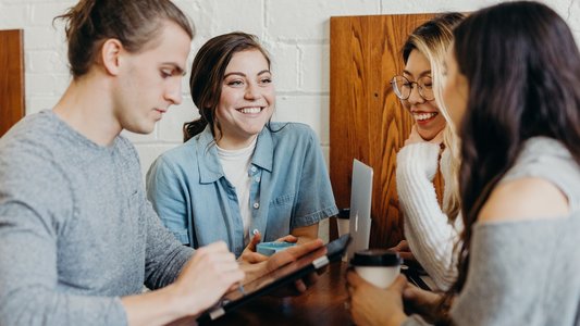 Drei Studentinnen und ein Student sitzen im Café und reden miteinander.