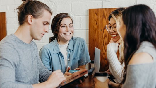 Drei Studentinnen und ein Student sitzen im Café und reden miteinander.