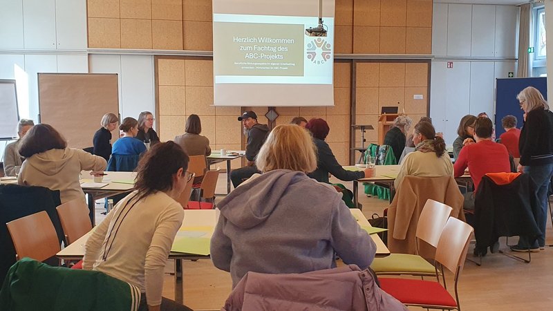 Frauen und Männer sitzen an mehreren Tischen und tauschen sich aus.