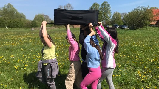 Mehrere Kinder tragen gemeinsam einen schweren Koffer.