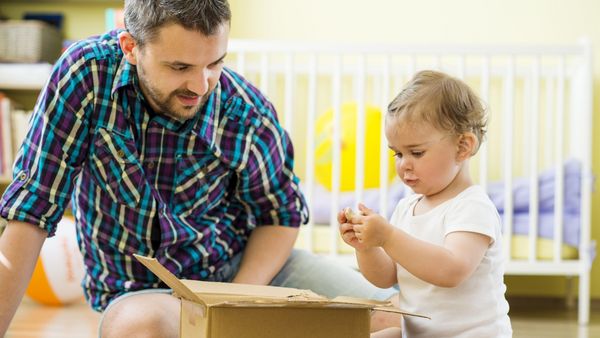 Ein Mann und ein kleines Kind sitzen auf dem Fußboden. Das Kind packt etwas aus einem Karton aus.