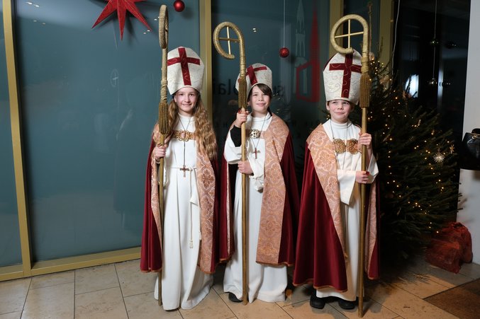 Die Kinderbischöfe Kira, Connor und Rike stehen im Ornat neben einem Tannenbaum.