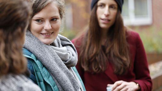 Drei junge Frauen stehen vor der Hochschule und unterhalten sich.