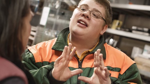 Ein junger Mann im Overall erklärt etwas.