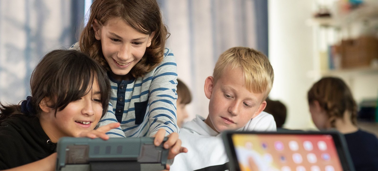 Schülerin und zwei Schüler arbeiten mit iPads in der 6. Klasse der STS