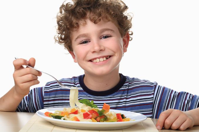 Ein fröhlicher Junge sitzt vor einem Teller Nudeln.