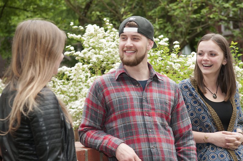 Zwei Studentinnen und ein Student der Hochschule lehnen an einer Mauer im Grünen.
