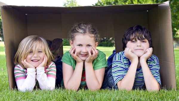 Zwei Mädchen und ein Junge liegen auf dem Rasen in einem Pappkarton.