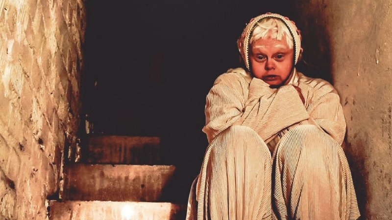 Eine als Gespenst verkleidete Frau sitzt auf einer Treppe.